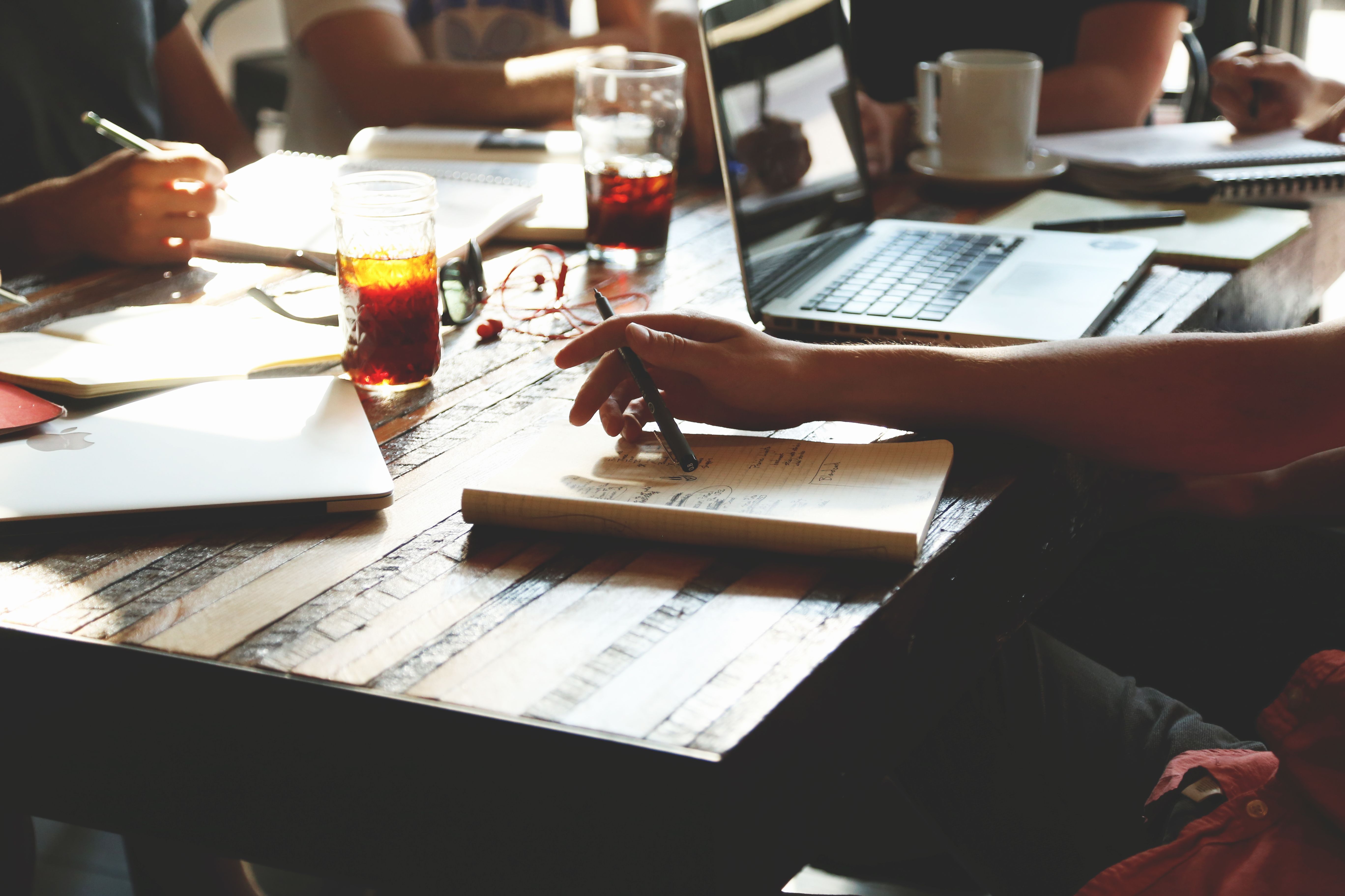 Team collaborating around a wooden table with notebooks, laptop, and coffee